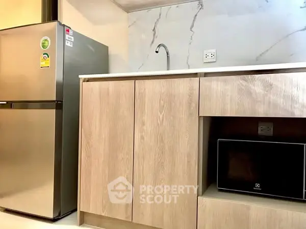 Modern kitchen with sleek cabinets, stainless steel fridge, and built-in microwave.