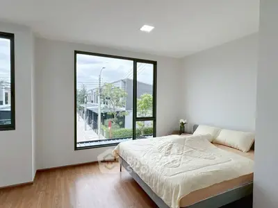 Bright and airy bedroom with large windows offering a street view, featuring a cozy bed and modern decor.
