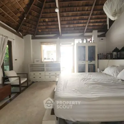 Spacious bedroom with rustic wooden ceiling and natural light, featuring a cozy bed and elegant decor.