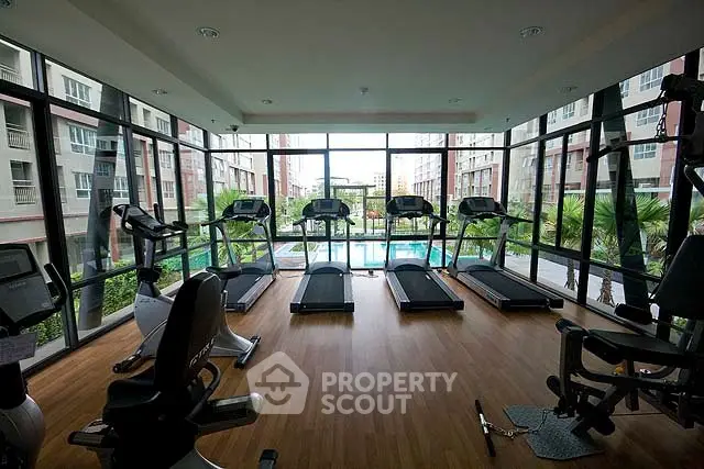 Modern gym with large windows overlooking a pool in a luxury apartment complex.