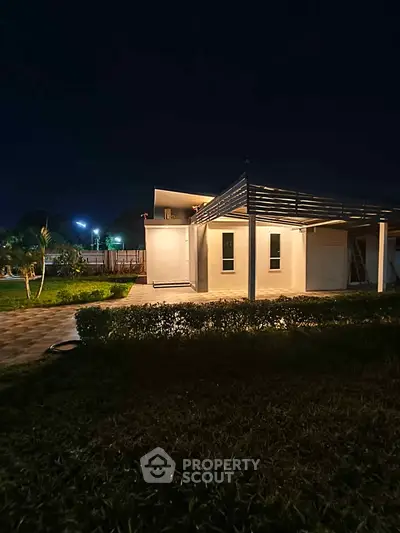 Modern house exterior with night lighting and lush garden view