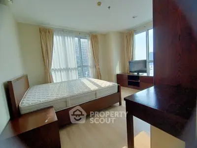 Spacious bedroom with large windows and city view, featuring wooden furniture and natural light.