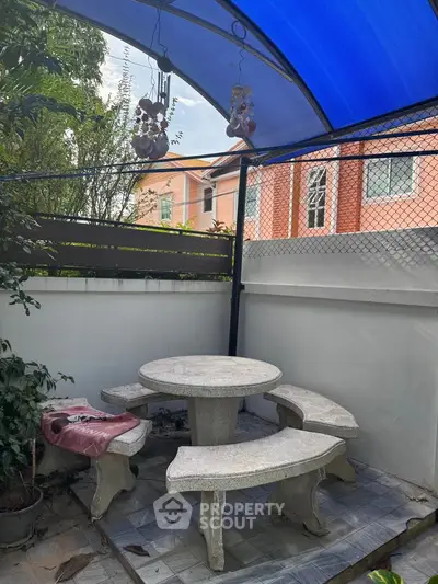 Charming outdoor patio with stone table and benches under a blue canopy, perfect for relaxation.