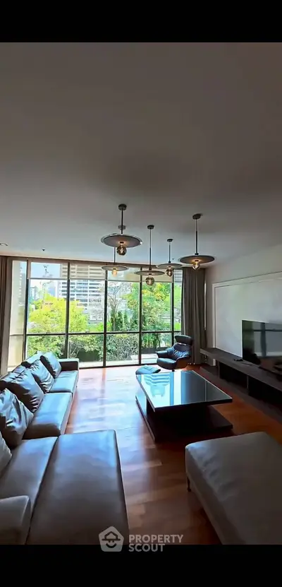 Spacious living room with modern decor and large windows offering a lush garden view.