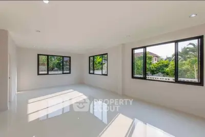 Spacious sunlit room with large windows and glossy floors, offering a serene garden view.