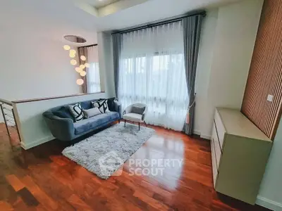 Elegant living room with modern decor, hardwood floors, and large window with sheer curtains.