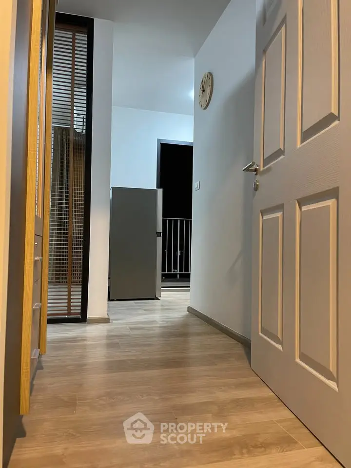 Modern apartment hallway with wooden flooring and open door leading to balcony.