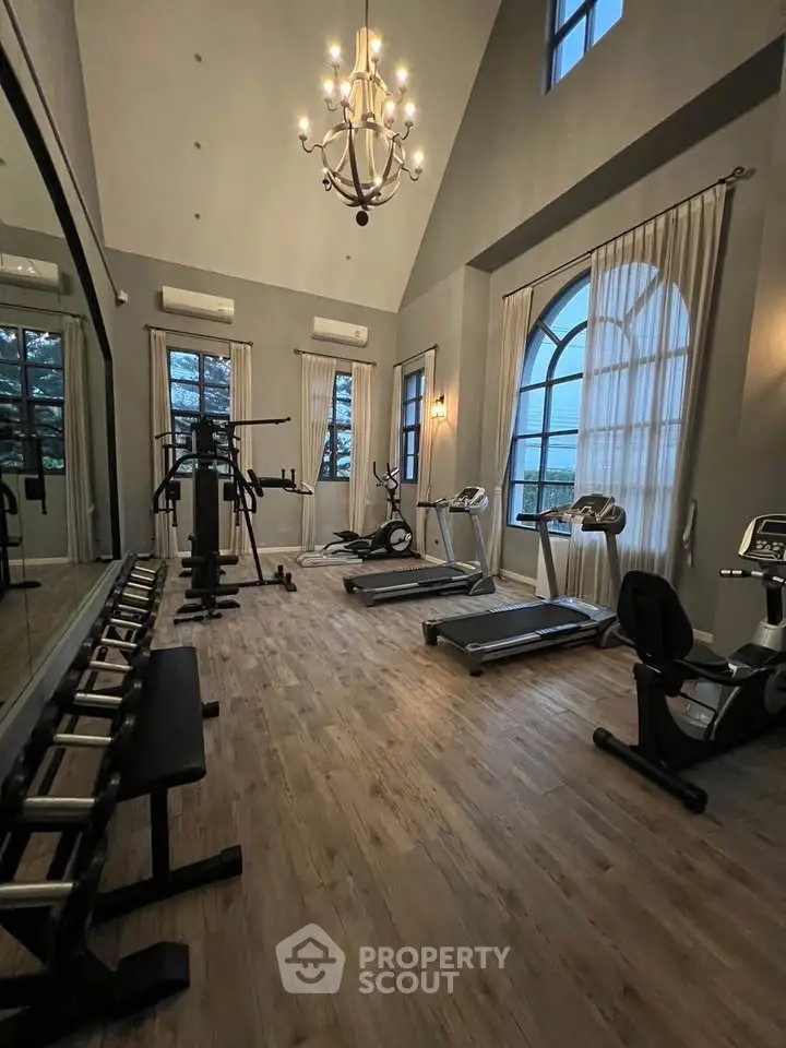 Luxurious home gym with high ceilings, elegant chandelier, and modern fitness equipment.