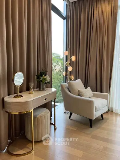 Elegant living room with plush armchair and vanity near large window with lush view.