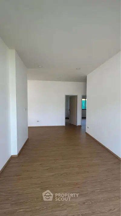 Spacious empty room with wooden flooring and white walls, ideal for customization.