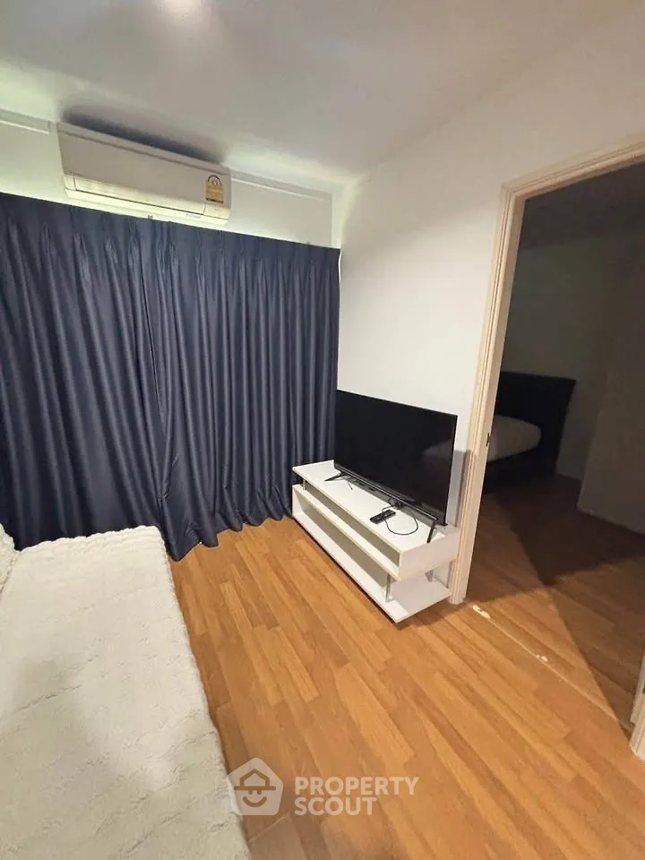 Cozy living room with wooden flooring, modern TV setup, and elegant curtains.