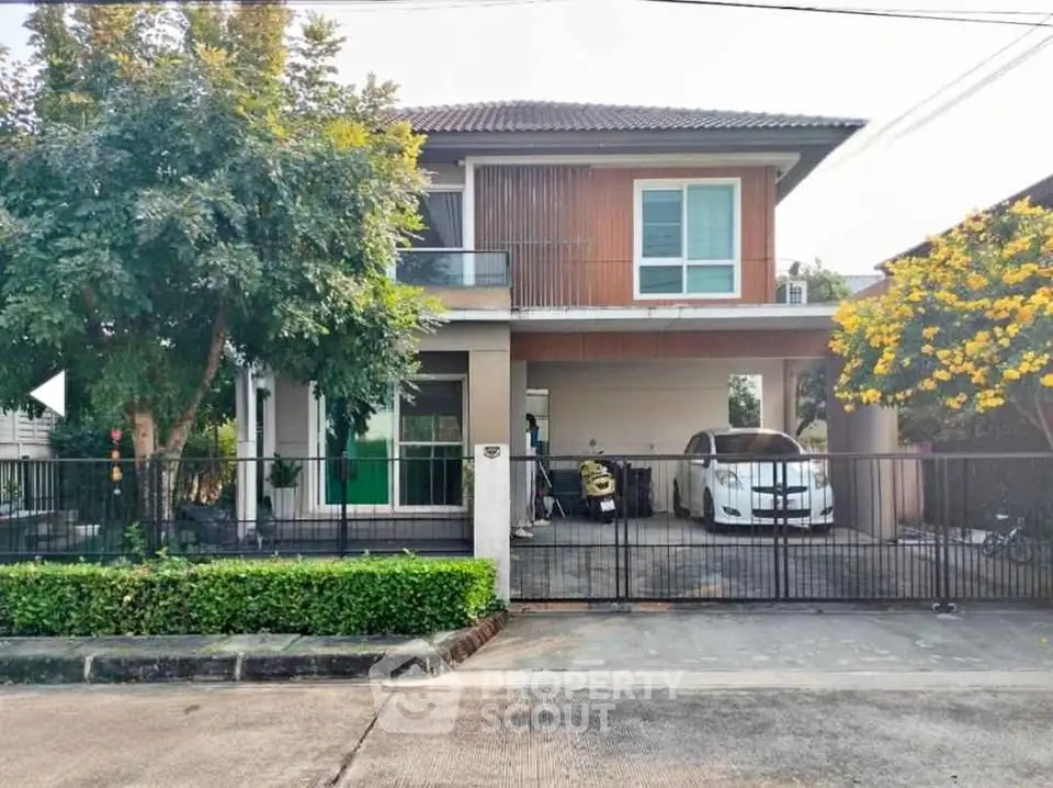 Charming two-story house with carport and lush greenery in a serene neighborhood.