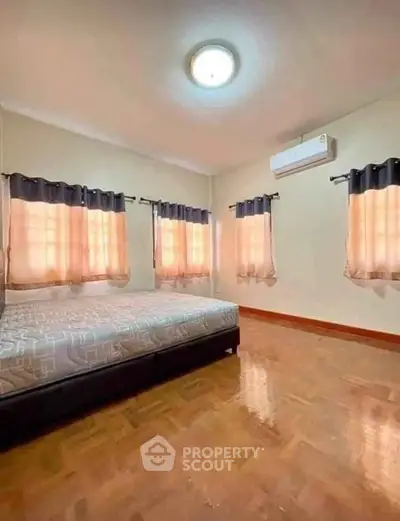 Spacious bedroom with wooden flooring and ample natural light from multiple windows.