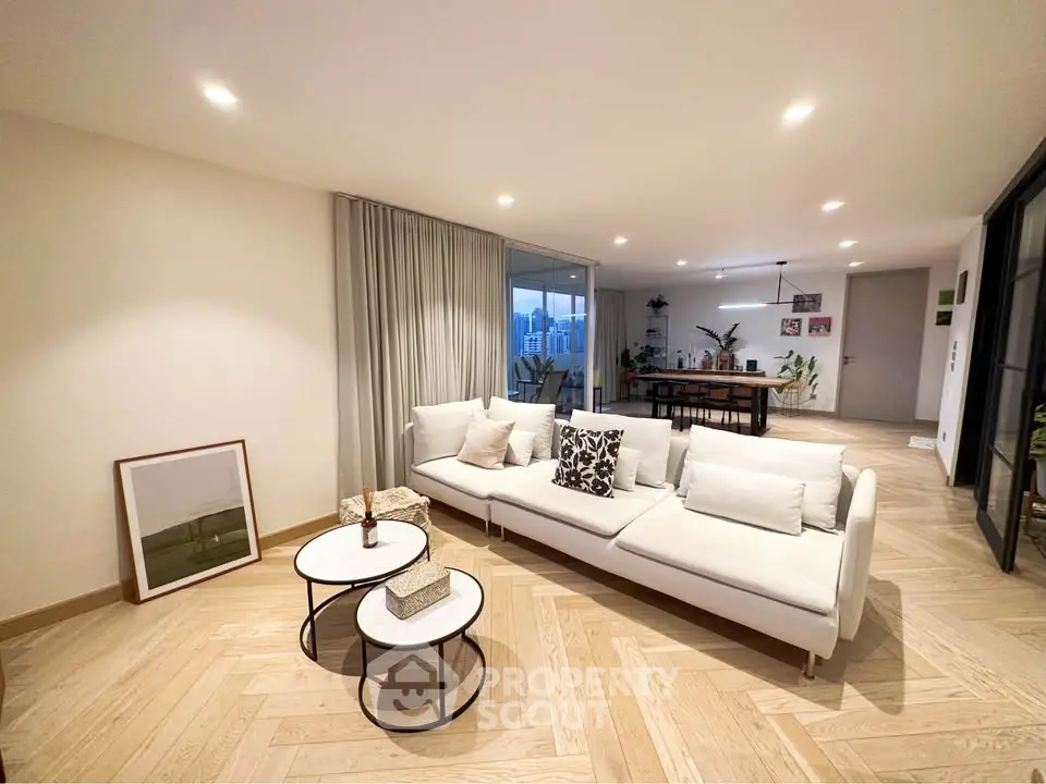 Spacious modern living room with elegant decor and city view, featuring a cozy white sofa and stylish coffee tables.