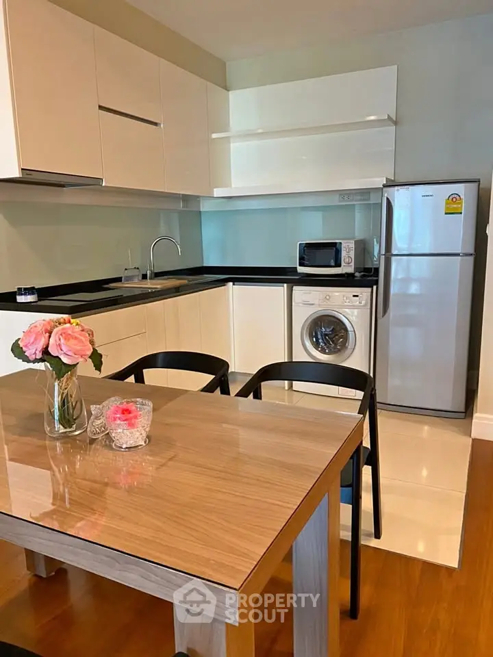 Modern kitchen with sleek cabinets, dining table, and appliances including fridge and washing machine.