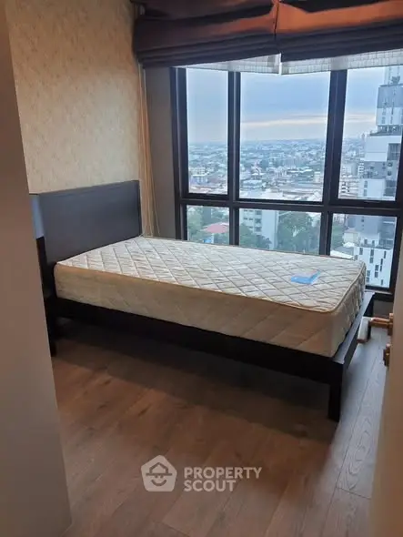 Cozy bedroom with large window offering stunning city views, featuring a single bed and wooden flooring.