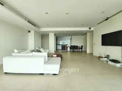 Spacious modern living room with white sectional sofa and wall-mounted TV, open layout to dining area.