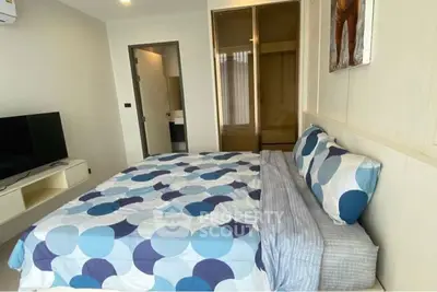 Modern bedroom with stylish bedding and wall art, featuring a sleek TV setup and ample natural light.