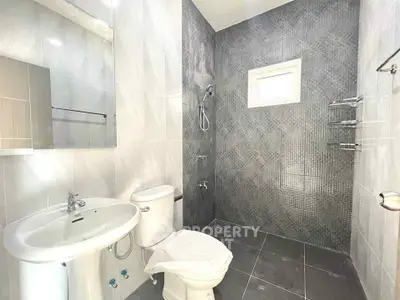 Modern bathroom with sleek gray tiles and white fixtures, featuring a shower area and natural light.