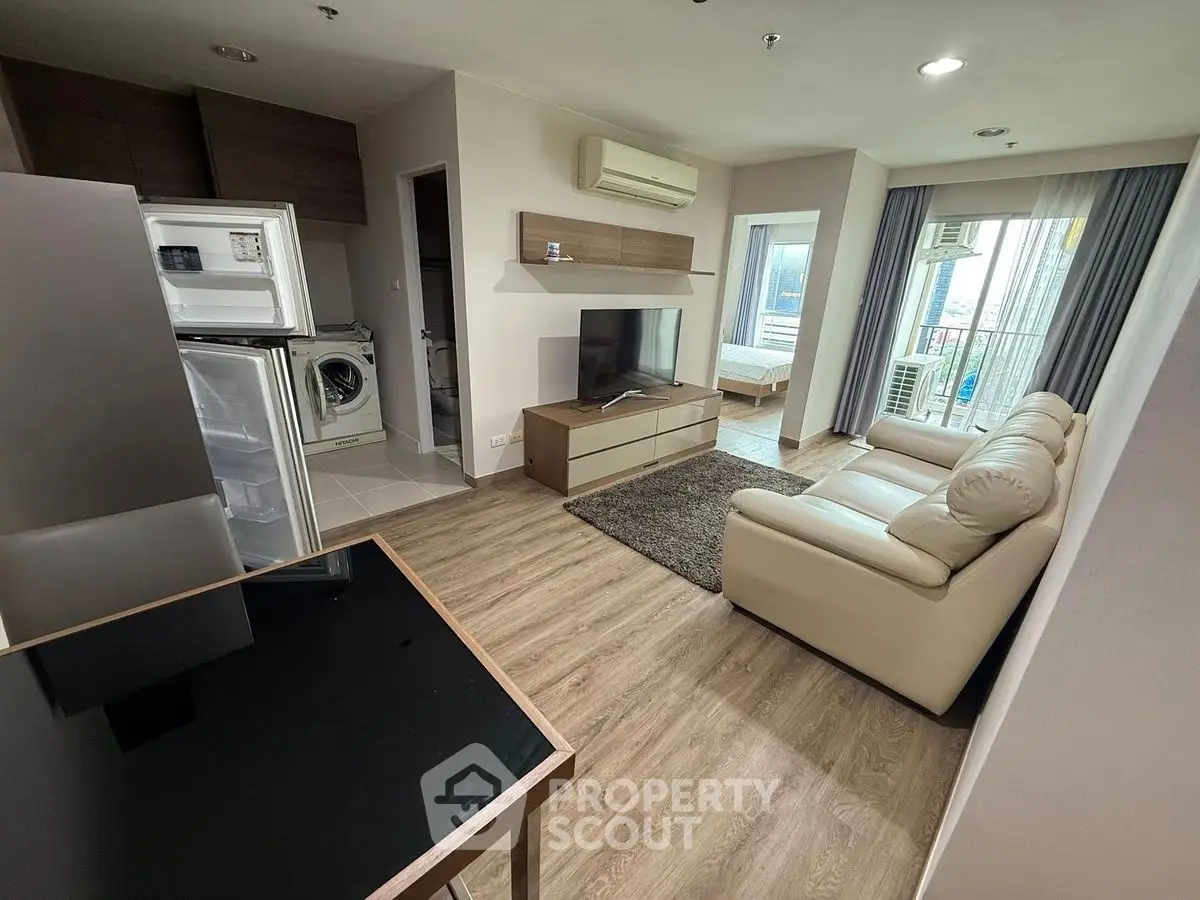 Modern living room with open kitchen, featuring sleek furniture and appliances.