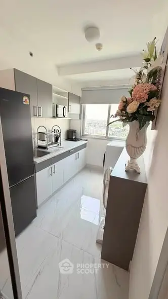 Modern kitchen with sleek cabinets, large fridge, and elegant floral arrangement, offering a bright and airy space.