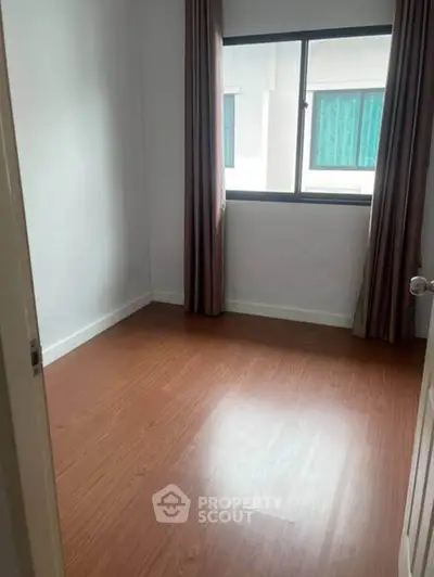 Cozy empty room with wooden flooring and large window, perfect for customization.