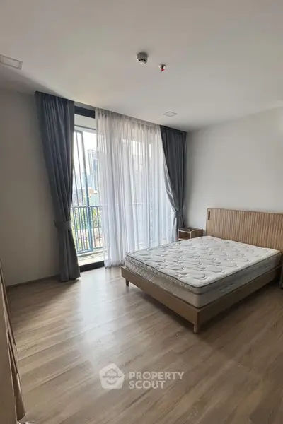 Spacious bedroom with large window and city view, featuring modern minimalist design and wooden flooring.