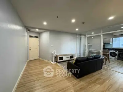 Modern living room with sleek wooden flooring and open kitchen layout, featuring a cozy black sofa and stylish decor.