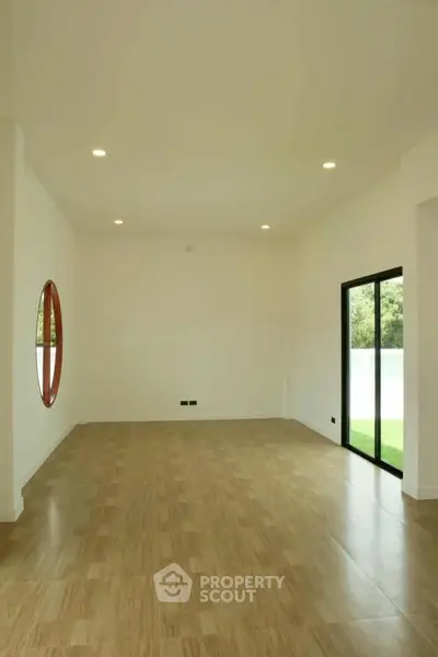 Spacious modern living room with wooden flooring and large window view.