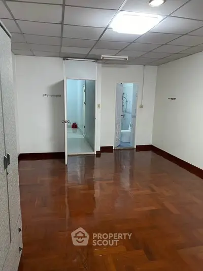 Spacious empty room with wooden flooring and two doorways leading to bathrooms.