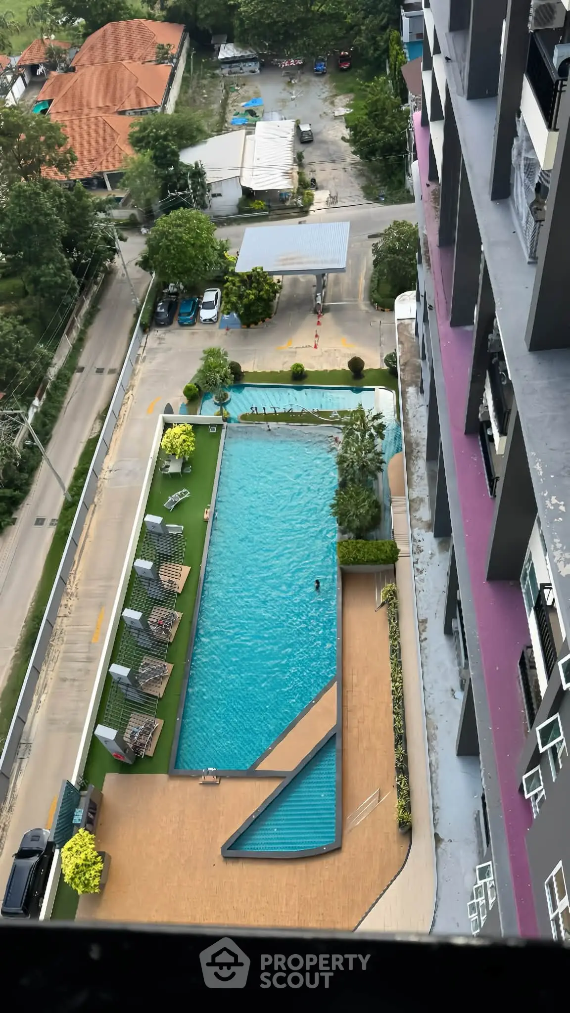 Stunning aerial view of modern apartment building with luxurious swimming pool and lush surroundings.