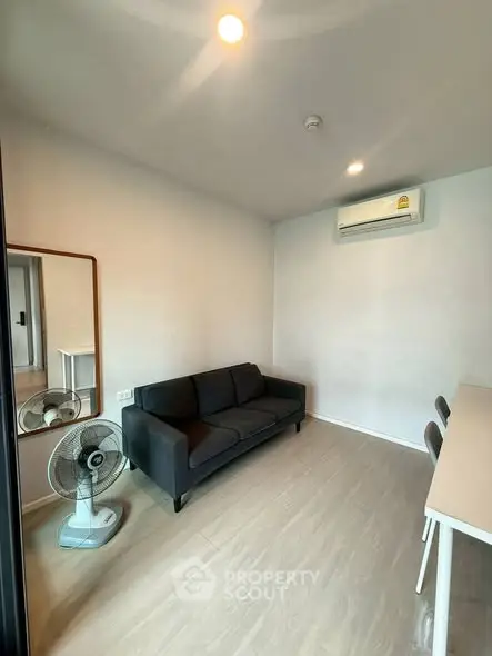 Modern living room with sleek black sofa, wall-mounted air conditioner, and minimalist decor.