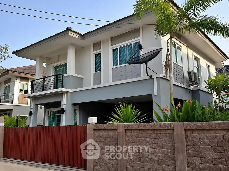 Modern two-story house with balcony and lush garden in a serene neighborhood.