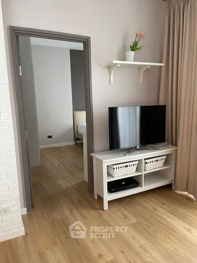 Modern living room with TV stand and wooden flooring, leading to a cozy bedroom.