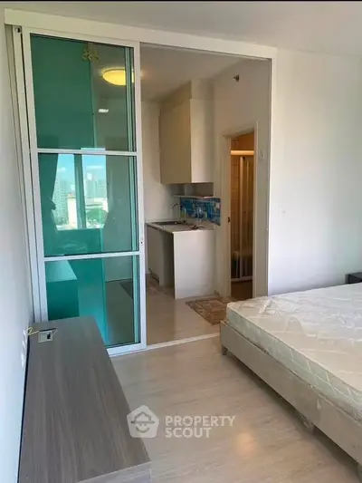 Modern apartment bedroom with sliding glass door to compact kitchen and city view window.