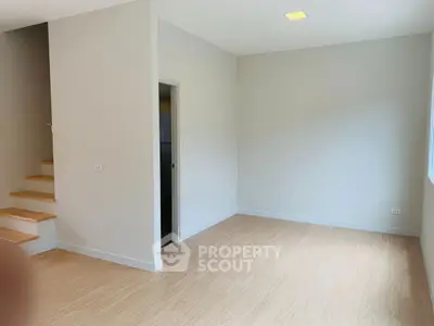 Spacious empty room with wooden flooring and staircase, ideal for customization.