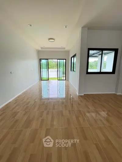 Spacious living room with large windows and glossy wooden flooring, perfect for natural light and modern living.