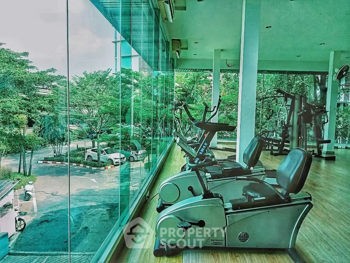 Modern gym with large windows offering lush green views, featuring exercise bikes and fitness equipment.
