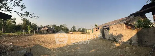 Expansive land plot with potential for development, surrounded by rustic buildings and lush greenery.