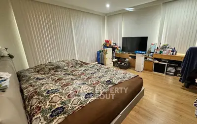 Spacious bedroom with modern decor and large windows, featuring a cozy bed and entertainment setup.