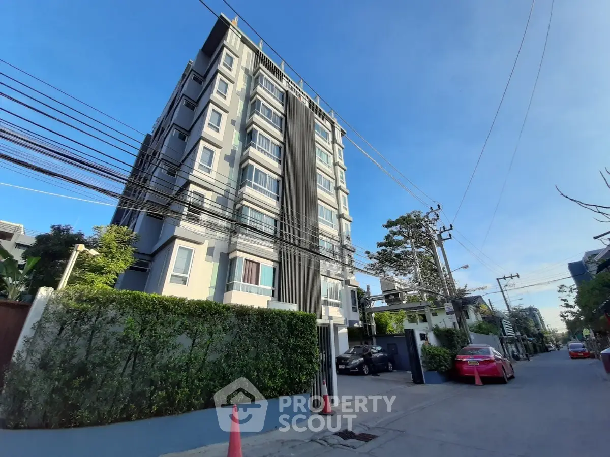 Modern multi-story residential building with lush greenery and clear blue sky.