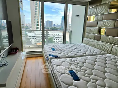 Modern bedroom with twin beds and city view from large windows in high-rise apartment.