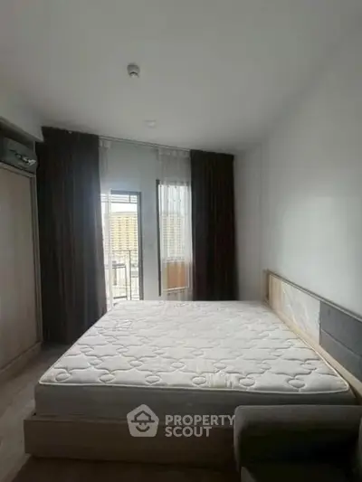 Spacious bedroom with large window and modern furnishings in a high-rise apartment.