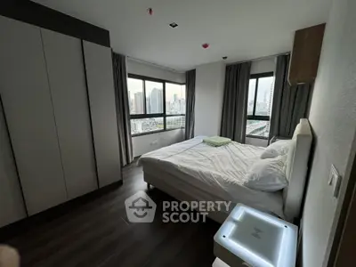 Modern bedroom with city view, featuring large windows and sleek furniture in a high-rise apartment.