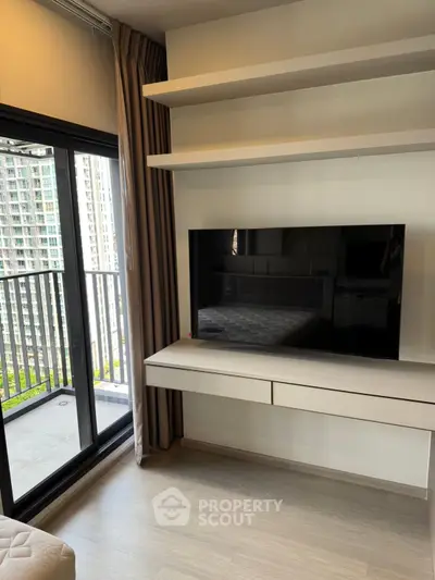 Modern living room with sleek TV setup and balcony view in high-rise apartment.