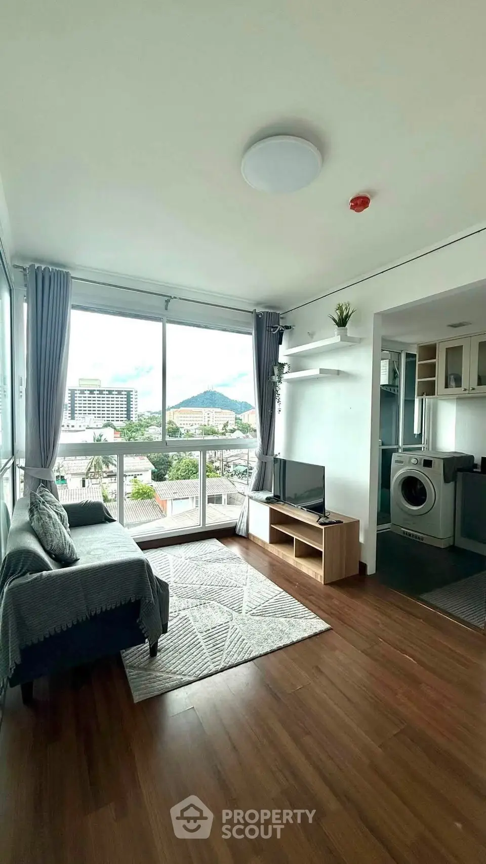 Modern living room with large windows and city view, featuring cozy seating and integrated kitchen area.