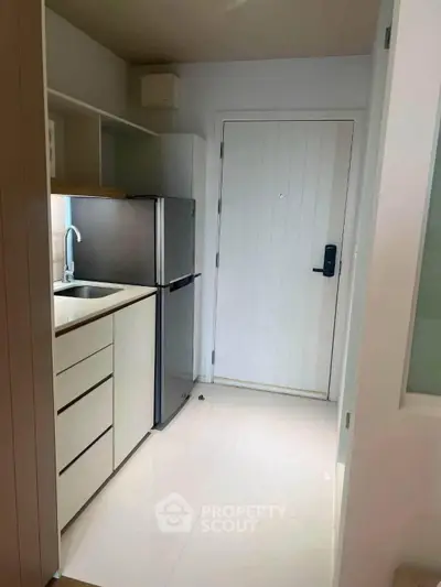 Modern compact kitchen with sleek cabinetry and stainless steel fridge in a cozy apartment.