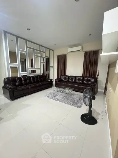 Spacious living room with modern leather sofas and stylish mirrored wall design.