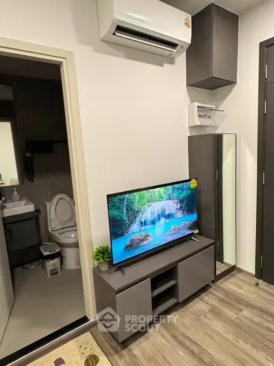 Modern living room with sleek TV unit and air conditioning, adjacent to a compact bathroom.