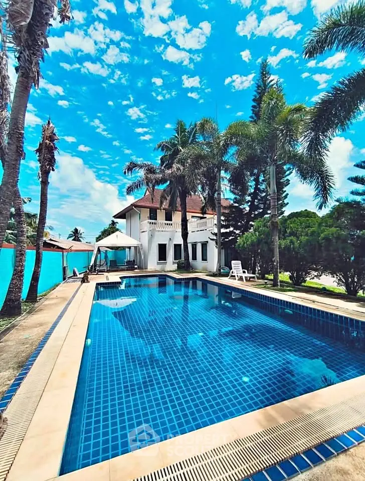 Luxurious villa with a stunning pool surrounded by palm trees and clear blue skies.